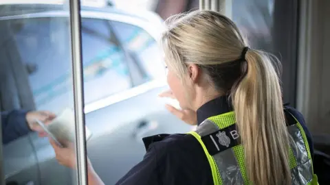 Border Force officer checks persons passport through booth window