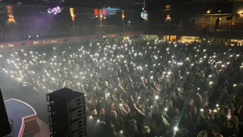 Gliderdrome A crowd watching the stage (out of view to the left) are holding up lights on their mobile phones in front of Scouting for Girls