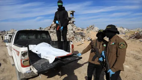 Reuters Hamas and Palestinian Islamic Jihad fighters stand next to a body bag that they say contains the remains of one of the last two dead hostages, in Beit Lahia, northern Gaza (3 December 2025)