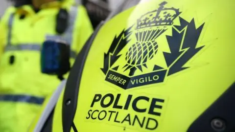 Police Scotland logo on a yellow background with an officer in the background.