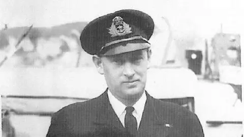 Coastal Forces Heritage Trust A naval officer is depicted in black and white looking straight toward the camera and wearing an official hat and suit. 