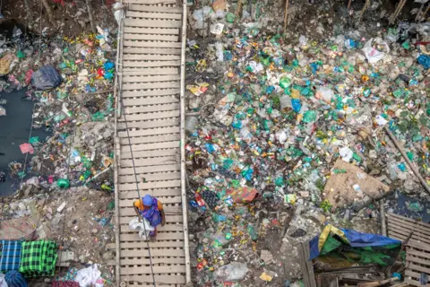 MONIRUL ALAM/EPA A woman walks on the wooden bridge next to a Kajla canal filled with household garbage in Dhaka, Bangladesh