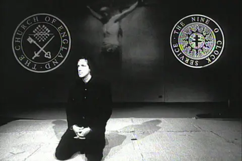 Jon Jones A black-and-white image shows Chris Brain wearing dark clothing as he kneels on the floor, his hands in his lap. Behind him is an image of Jesus on the cross as well as the Church of England and Nine O'Clock Service logos.