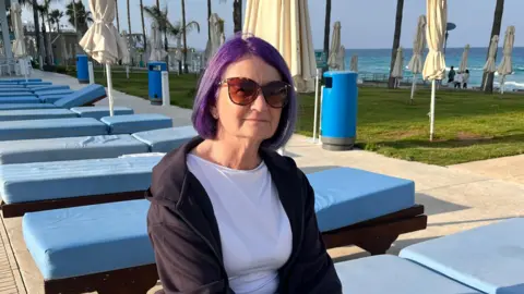 British ex-pat Victora O'ffe sitting on a lounge chair with multiple empty lounge chairs from behind