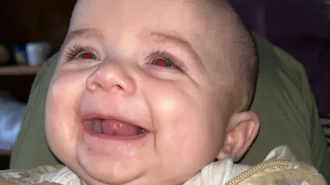 Jensen-Lee laughing in a close up shot. His mouth is open as he smiles. His head is resting on a green pillow. 