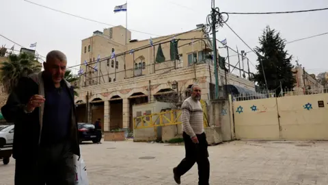 Palestinians walk in front of an Israeli settlement in the old city in Hebron, in the occupied West Bank (9 February 2026)