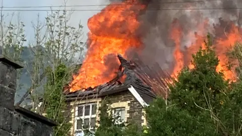 Abandoned school building with it's roof on fire and visibly collapsed