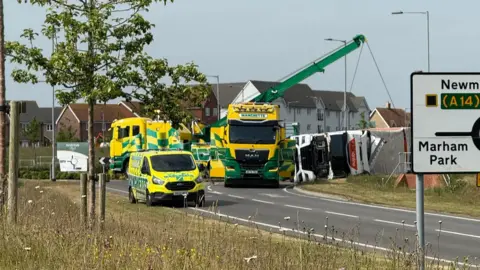 Bex Ivy-Marie Guy A specialist lorry with a crane on it lifts the overturned lorry off the road. Other recovery vehicles are parked nearby.