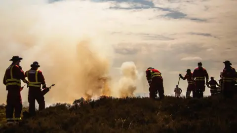 Eight firefighters in silhouette, putting out a countryside wildfire.