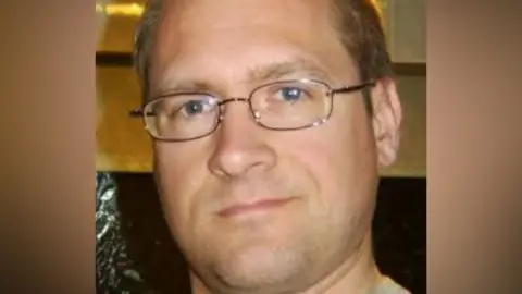 Family photograph Close-up shot of a bespectacled man with light brown hair. He is looking directly at the camera.
