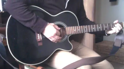 Devon and Cornwall Police A person holding a black guitar on their lap and sat down.