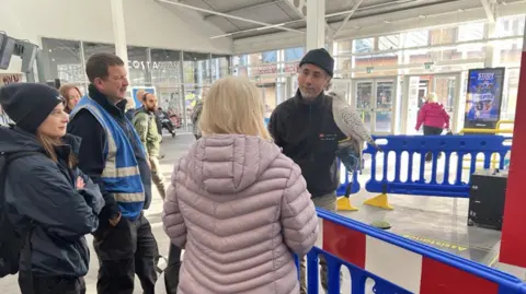Greater Anglia A small crowd of people in a railway station watching intently as a man with a white bird speaks to them
