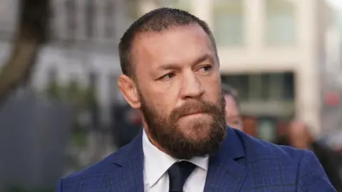 PA Media McGregor is wearing a navy suit and has a brown beard.