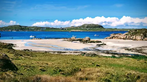 Mark Berry A view of a sunny beach, with an island in the distance.