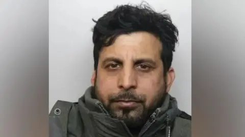 National Crime Agency A mugshot of Shahid Hussain who has dark hair, brown eyes and a beard. He appears to be wearing a thick coat.