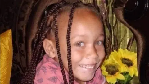 Joshlin Smith, with her hair in plaits and wearing a pink top, smiles at the camera