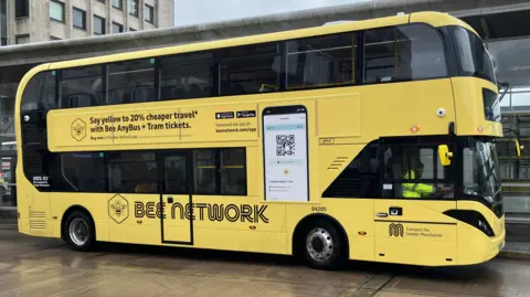 A yellow and black liveried Bee Network bus stands at a bus station stop