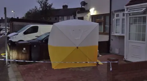 PA Media An image of a yellow and white police forensics tent outside a property in First Avenue, Dagenham