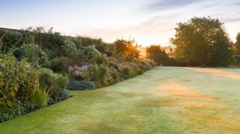 Goldstone Hall Hotel & Gardens A lush green lawn, surrounded by foliage and different flowers on the left hand side.