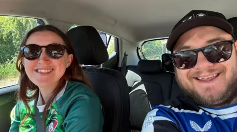 Supplied Woman with Leicester Tigers top and man in Bath top, both wearing sunglasses, sitting in a car