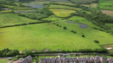 An aerial view of the green fields with a row of houses in front