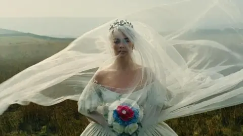 Warner Bros Australian actor Margot Robbie wearing a white wedding dress and holding a bouquet of flowers pictured on moorland in the Yorkshire Dales National Park