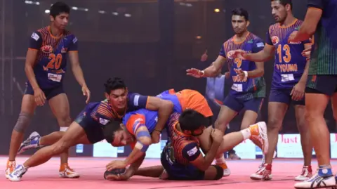 West Midlands Growth Company Male kabaddi players tackle opponents with some on the floor and others standing. They are all dressed in shorts and tops.