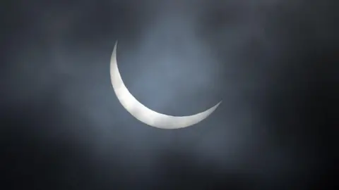 The sun obscuring the moon on a dark, cloudy night. 
