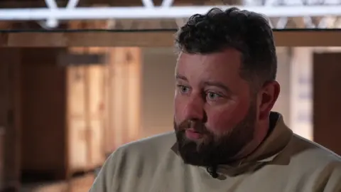 Danny Bowcock, wearing a beige jumper with a brown shirt underneath