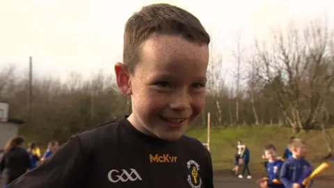 A young boy with short brown hair and freckles wearing a black GAA sports top