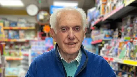 An elderly man with grey hair and a blue jacket