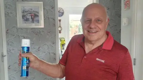 Man in red polo shirt holding can of fly spray and smiling at the camera