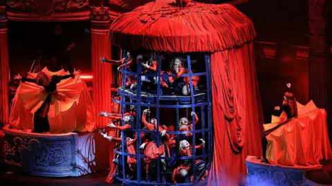 Getty Images Dancers dressed in red costumes in a cage, wrapped in red material, onstage at Lady Gaga performance in Rio