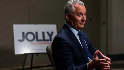 Imagen de archivo de Getty Images de David Jolly, quien viste un traje y está sentado con las manos entrelazadas frente a un cartel que dice: "Jolly para gobernador".