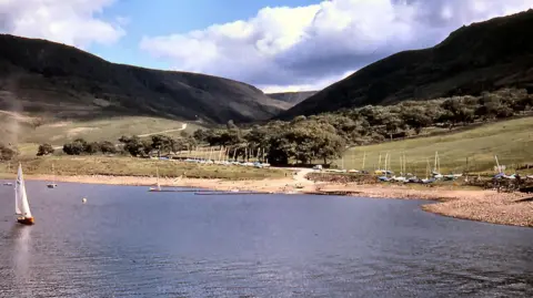 A lone vessel sails on Dovestones Reservoir with hills and a valley in the background.