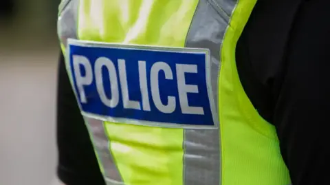 The back view of a British police officers vest. It is bright yellow and says the words POLICE in bold white lettering 