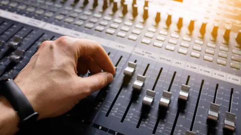 A hand adjusting the knobs and faders on an audio mixer