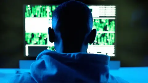 Rear view of a male model in a hoodie in front of a computer in South Africa