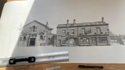 Simon Spark/BBC A long roll of paper with highly-detailed and life-like drawings of two old buildings including a pub which says 'Prince of Wales Inn' above it. A ruler and pen can be seen underneath it.