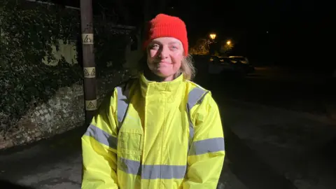 Emily Coady-Stemp/BBC Vanessa Rowlands looks at the camera and smiles. She is wearing a red beanie hat and a high viz jacket.