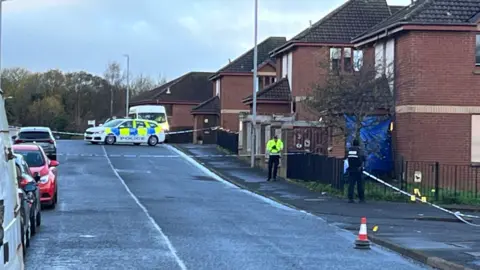 A cordoned off residential street with a police car and police van