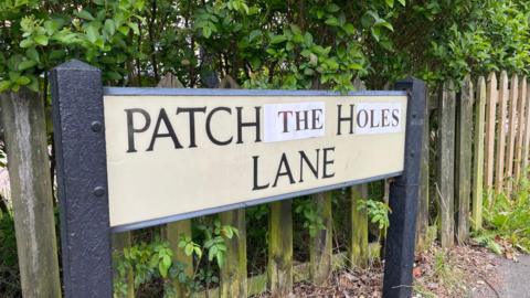 A road sign that reads: "Patch the holes lane"