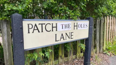 Tom Larsen-Wright/BBC A road sign that reads: "Patch the holes lane"