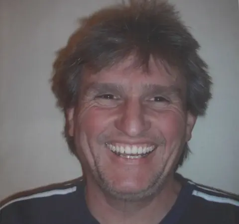 Charlotte Lunn A man with brown hair and t-shirt with stripes on the shoulders smiles at the camera