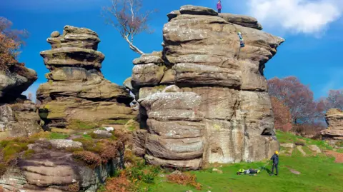 Dark_Eni/Getty A large rock formation with a person at the bottom and someone, about 30ft higher, at the top