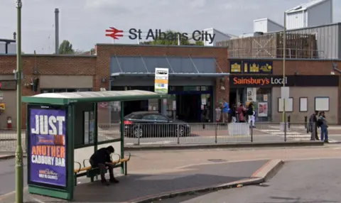 Google The main entrance to St Albans City train station with a bus stop in the foreground and a Sainsbury's local supermarket in the background.