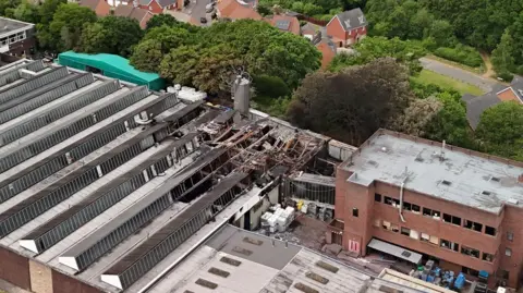 A picture taken with a drone, showing part of the fire-damaged factory, with homes behind it, divided by trees.