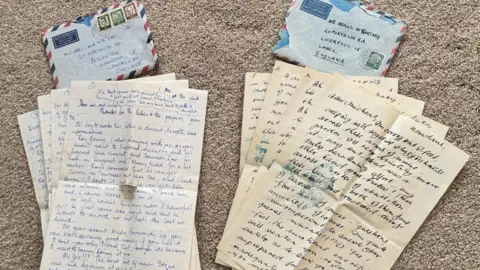 Mike McCartney A number of handwritten letters are piled on the floor with two envelopes. 