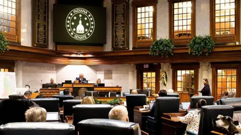 Members of the Indiana Senate are seen gathering in the chambers. 