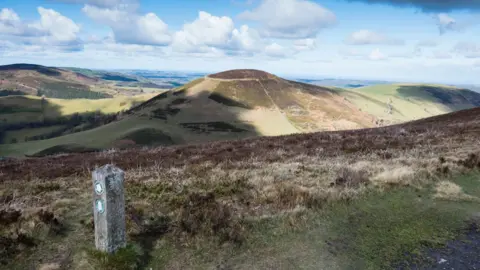 Getty Images Moel Arthur Iron-Age hill fort with a footpath pillar post in the foreground, heather, and then the hill of Moel Arthur with rolling open land behind it